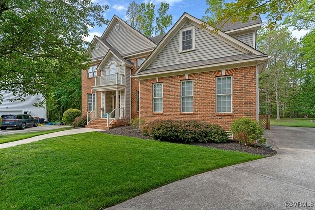 traditional-style home featuring concrete driveway, a front yard, brick siding, and a balcony
