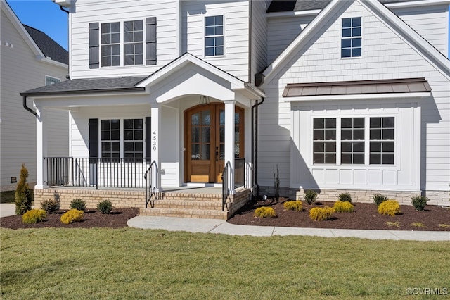 doorway to property with a yard, a shingled roof, and covered porch