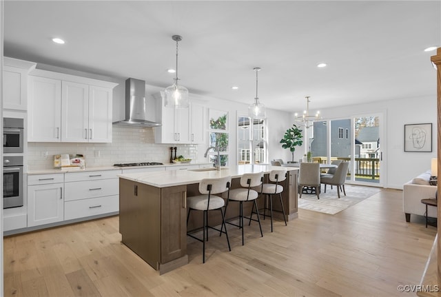 kitchen featuring stainless steel double oven, a sink, decorative backsplash, wall chimney exhaust hood, and light countertops