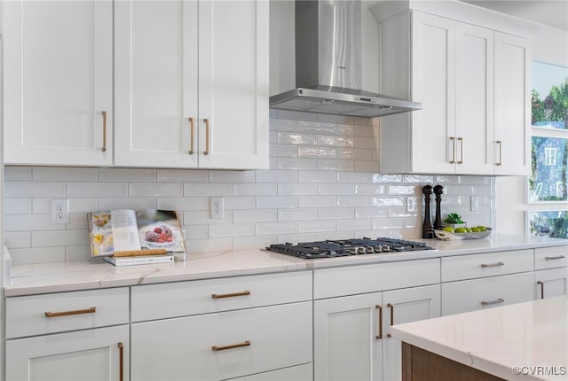 kitchen featuring wall chimney exhaust hood, stainless steel gas stovetop, decorative backsplash, and white cabinetry
