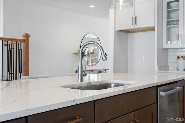 kitchen with white cabinetry, glass insert cabinets, a sink, dark brown cabinets, and light stone countertops