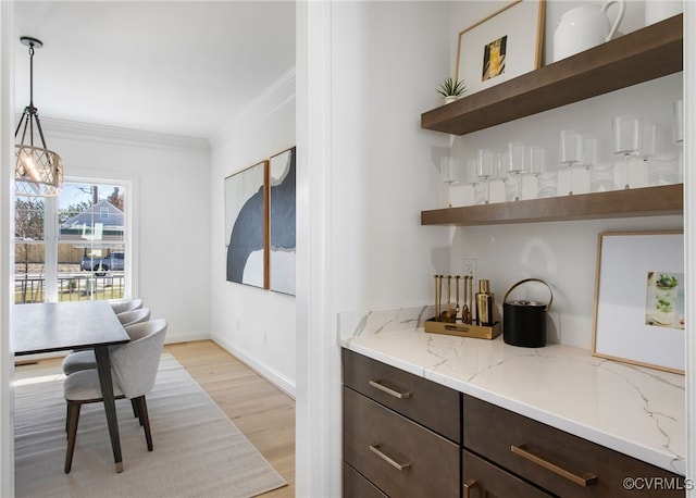 bar featuring crown molding, hanging light fixtures, baseboards, and light wood-type flooring
