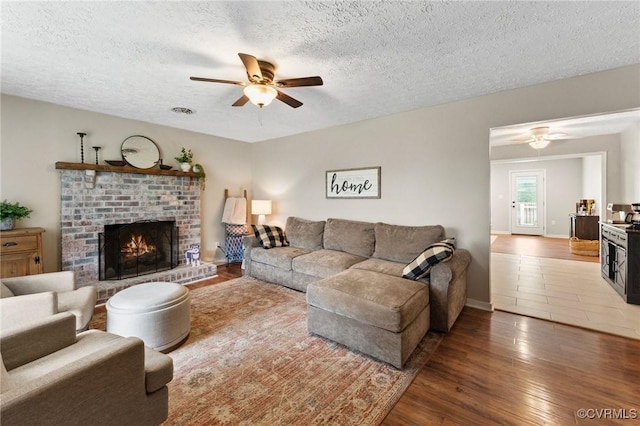 living area with a fireplace, wood finished floors, ceiling fan, and a textured ceiling