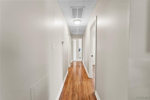 hall with attic access, visible vents, light wood-style flooring, and baseboards