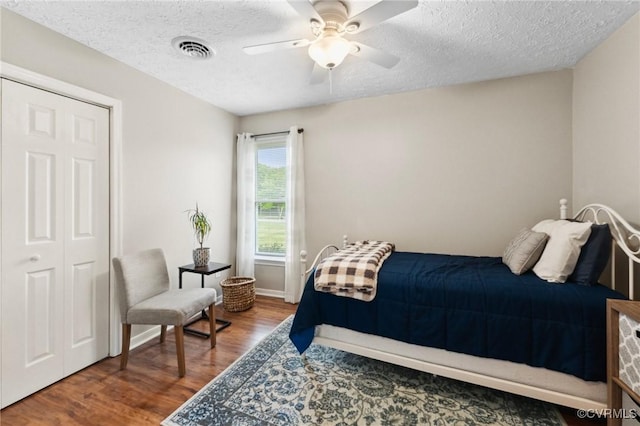 bedroom with wood finished floors, visible vents, a ceiling fan, and a textured ceiling