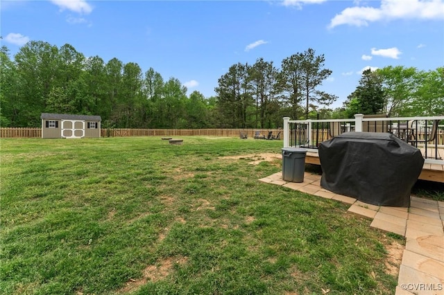 view of yard with an outbuilding, a wooden deck, a storage unit, and a fenced backyard