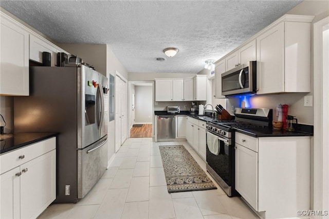kitchen with a sink, light tile patterned floors, white cabinetry, dark countertops, and appliances with stainless steel finishes