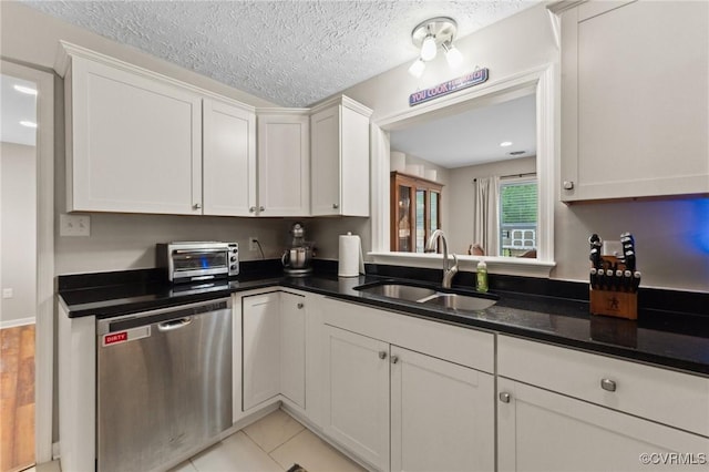 kitchen featuring a toaster, dark countertops, dishwasher, a sink, and white cabinetry