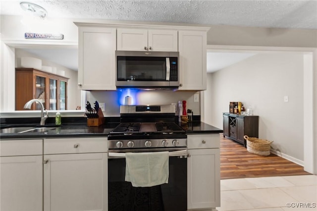 kitchen featuring dark countertops, stainless steel appliances, white cabinetry, and a sink