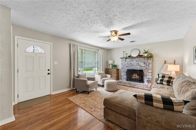 living room with wood finished floors, ceiling fan, a fireplace, baseboards, and a textured ceiling