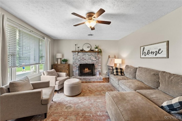living room featuring a brick fireplace, a textured ceiling, a ceiling fan, and wood finished floors