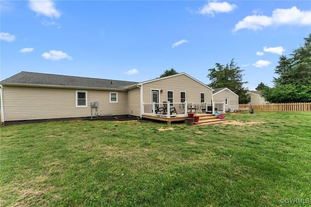 rear view of property featuring fence, a wooden deck, and a lawn