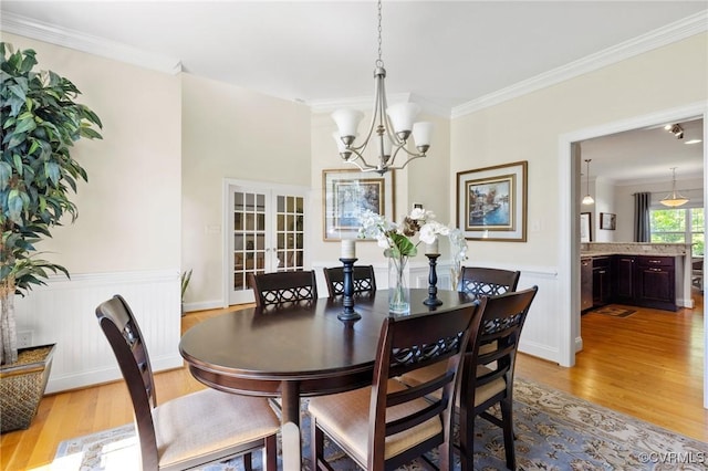 dining space with an inviting chandelier, crown molding, french doors, and light wood finished floors