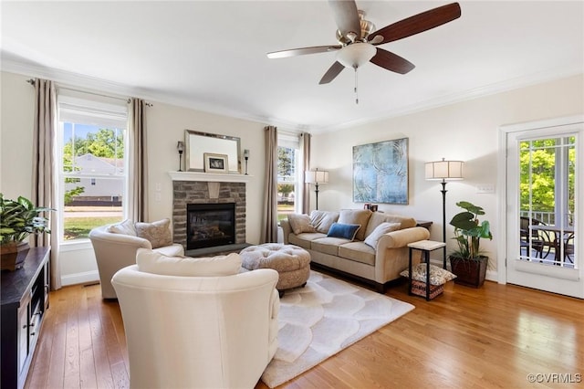 living room featuring light wood-style floors, ceiling fan, a stone fireplace, and a wealth of natural light
