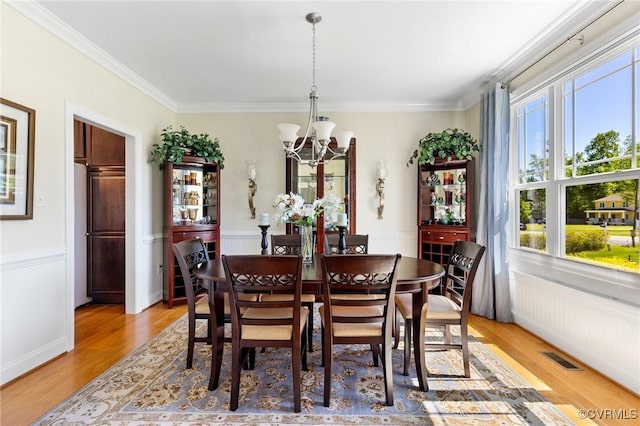 dining space with an inviting chandelier, crown molding, and light wood-style floors