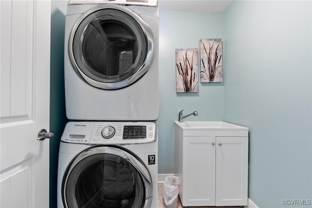 clothes washing area featuring a sink, baseboards, stacked washer and clothes dryer, and cabinet space