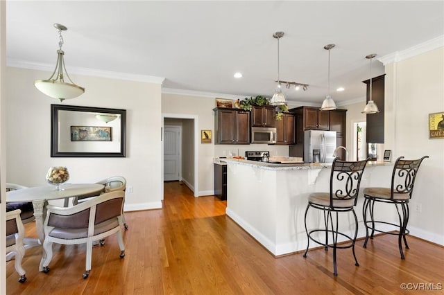 kitchen featuring dark brown cabinets, stainless steel appliances, a peninsula, a kitchen bar, and ornamental molding