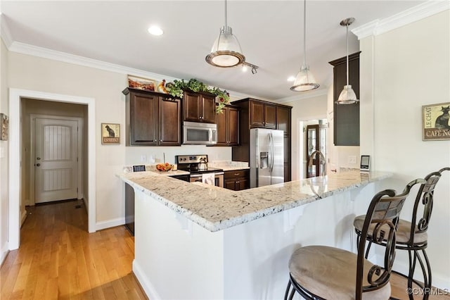 kitchen featuring crown molding, appliances with stainless steel finishes, dark brown cabinetry, and a breakfast bar area