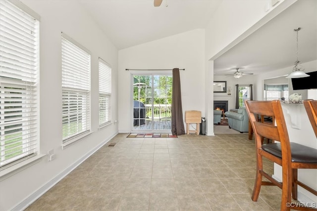 interior space featuring light tile patterned floors, a ceiling fan, a warm lit fireplace, and lofted ceiling