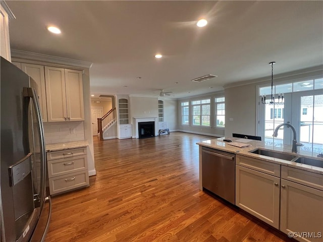 kitchen featuring crown molding, a fireplace, a sink, ceiling fan with notable chandelier, and stainless steel appliances