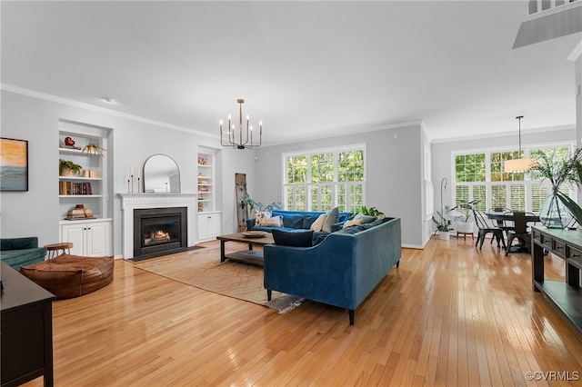 living room featuring crown molding, built in features, a fireplace with flush hearth, light wood-type flooring, and a notable chandelier