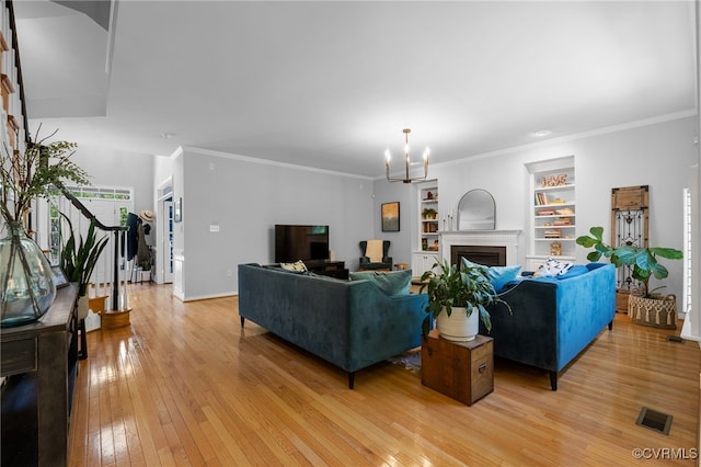 living room featuring visible vents, built in features, a fireplace, light wood-type flooring, and an inviting chandelier