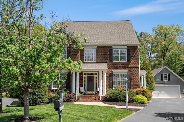 view of front facade featuring roof with shingles, brick siding, an outdoor structure, aphalt driveway, and a front lawn
