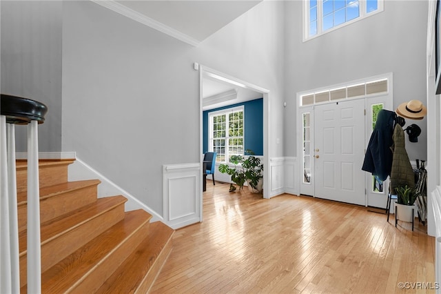 entryway featuring ornamental molding, light wood finished floors, a high ceiling, and stairway