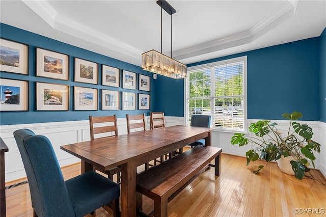 dining space with crown molding, wainscoting, a tray ceiling, and wood-type flooring