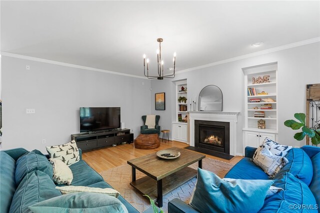 living room featuring an inviting chandelier, ornamental molding, wood finished floors, built in shelves, and a fireplace with flush hearth