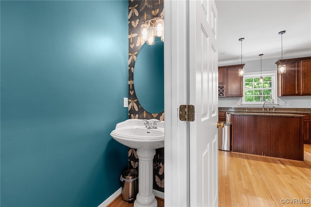bathroom featuring a sink, baseboards, crown molding, and wood finished floors