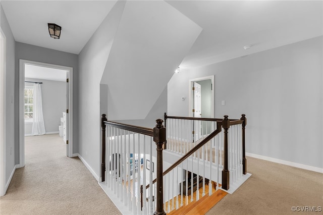 hall featuring carpet floors, baseboards, and an upstairs landing