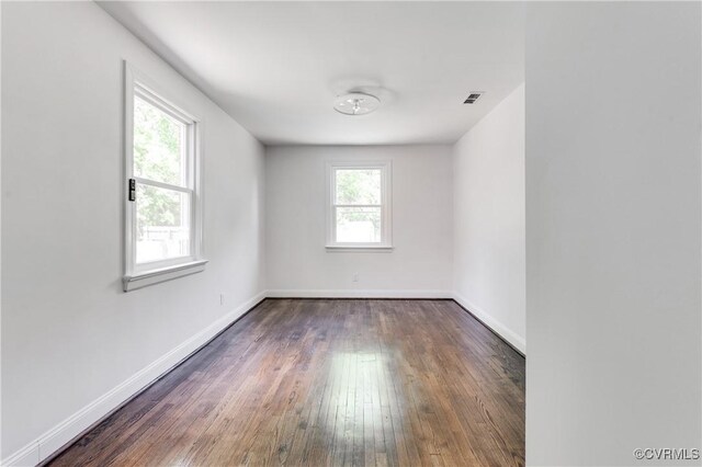 empty room with baseboards, visible vents, and hardwood / wood-style flooring