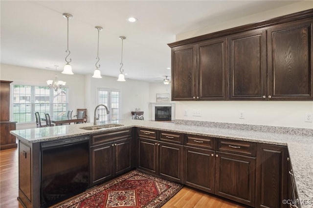 kitchen with a sink, black dishwasher, a glass covered fireplace, dark brown cabinetry, and light wood-style flooring