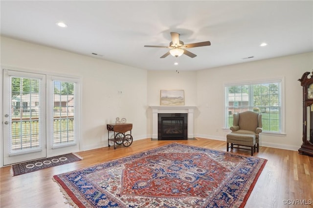 sitting room with wood finished floors, ceiling fan, plenty of natural light, and a glass covered fireplace