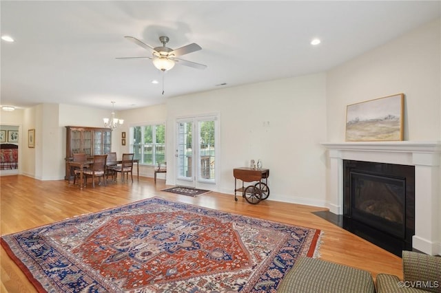 living room with recessed lighting, wood finished floors, ceiling fan with notable chandelier, baseboards, and a fireplace with flush hearth