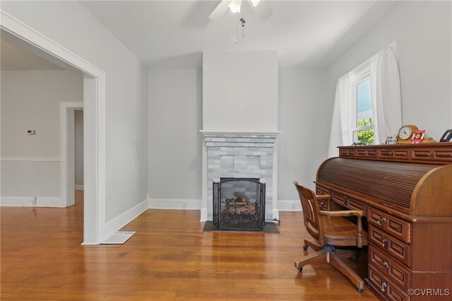 office area featuring wood finished floors, ceiling fan, a stone fireplace, and baseboards