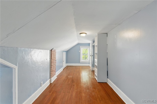 additional living space with baseboards, wood-type flooring, and vaulted ceiling