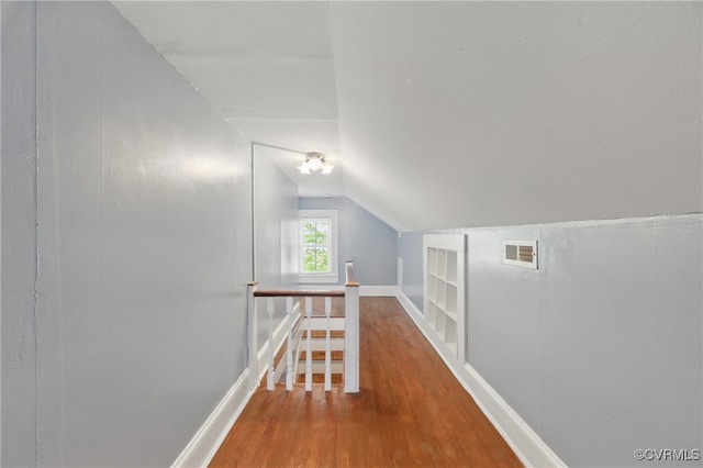additional living space with built in shelves, wood finished floors, visible vents, baseboards, and lofted ceiling
