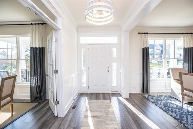 foyer entrance with a decorative wall, a chandelier, crown molding, visible vents, and dark wood-type flooring