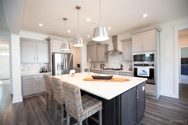 kitchen featuring wall chimney range hood, decorative backsplash, stainless steel appliances, dark wood-type flooring, and gray cabinets