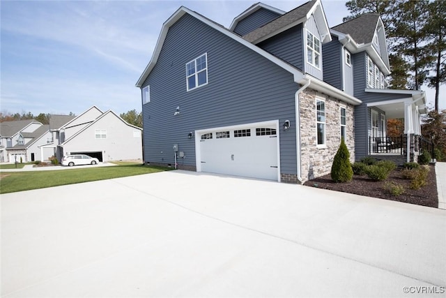 view of side of home featuring covered porch, concrete driveway, an attached garage, and stone siding