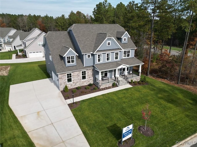 craftsman-style home with driveway, stone siding, roof with shingles, covered porch, and a front lawn