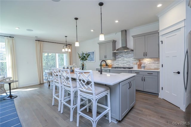 kitchen featuring a sink, a kitchen breakfast bar, tasteful backsplash, wall chimney range hood, and gray cabinetry
