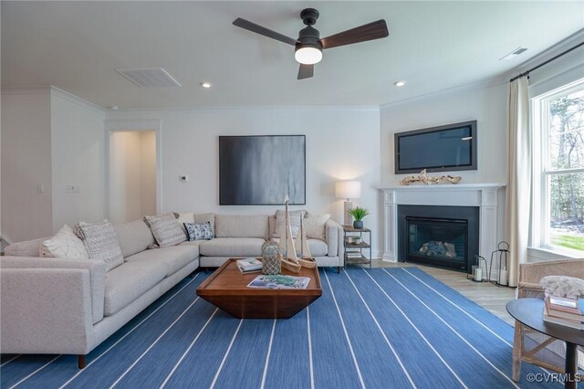 living area with visible vents, a ceiling fan, a fireplace with flush hearth, and crown molding
