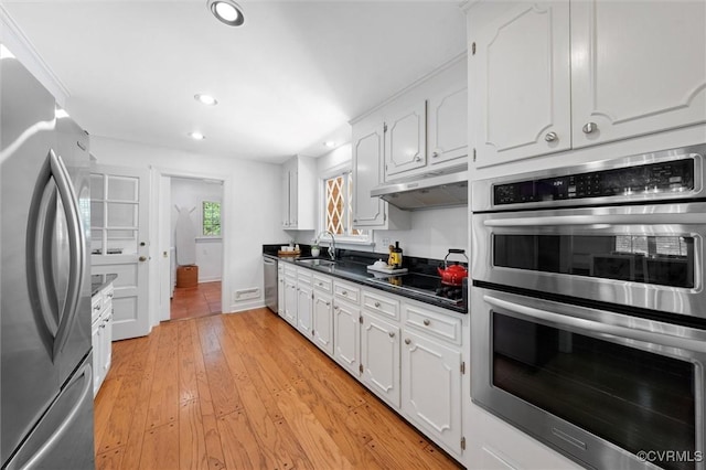 kitchen with dark countertops, appliances with stainless steel finishes, a sink, white cabinetry, and under cabinet range hood