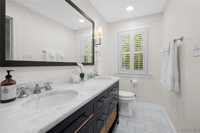 full bath with a sink, toilet, double vanity, marble finish floor, and baseboards