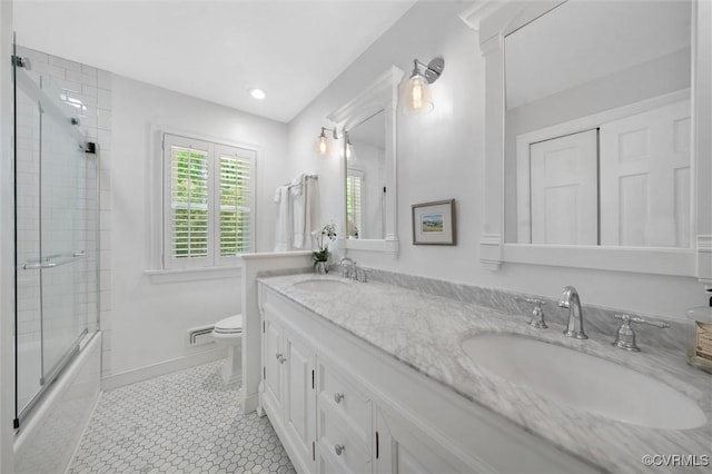 full bath featuring double vanity, toilet, a sink, and bath / shower combo with glass door