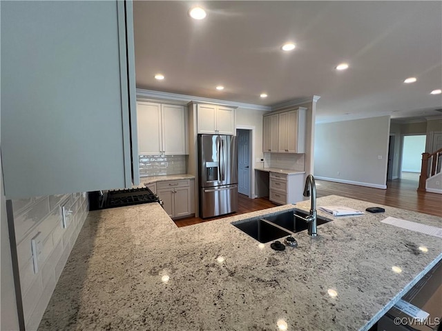 kitchen featuring a sink, light stone counters, ornamental molding, and stainless steel refrigerator with ice dispenser