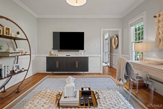living room with crown molding, a decorative wall, a wainscoted wall, and wood finished floors